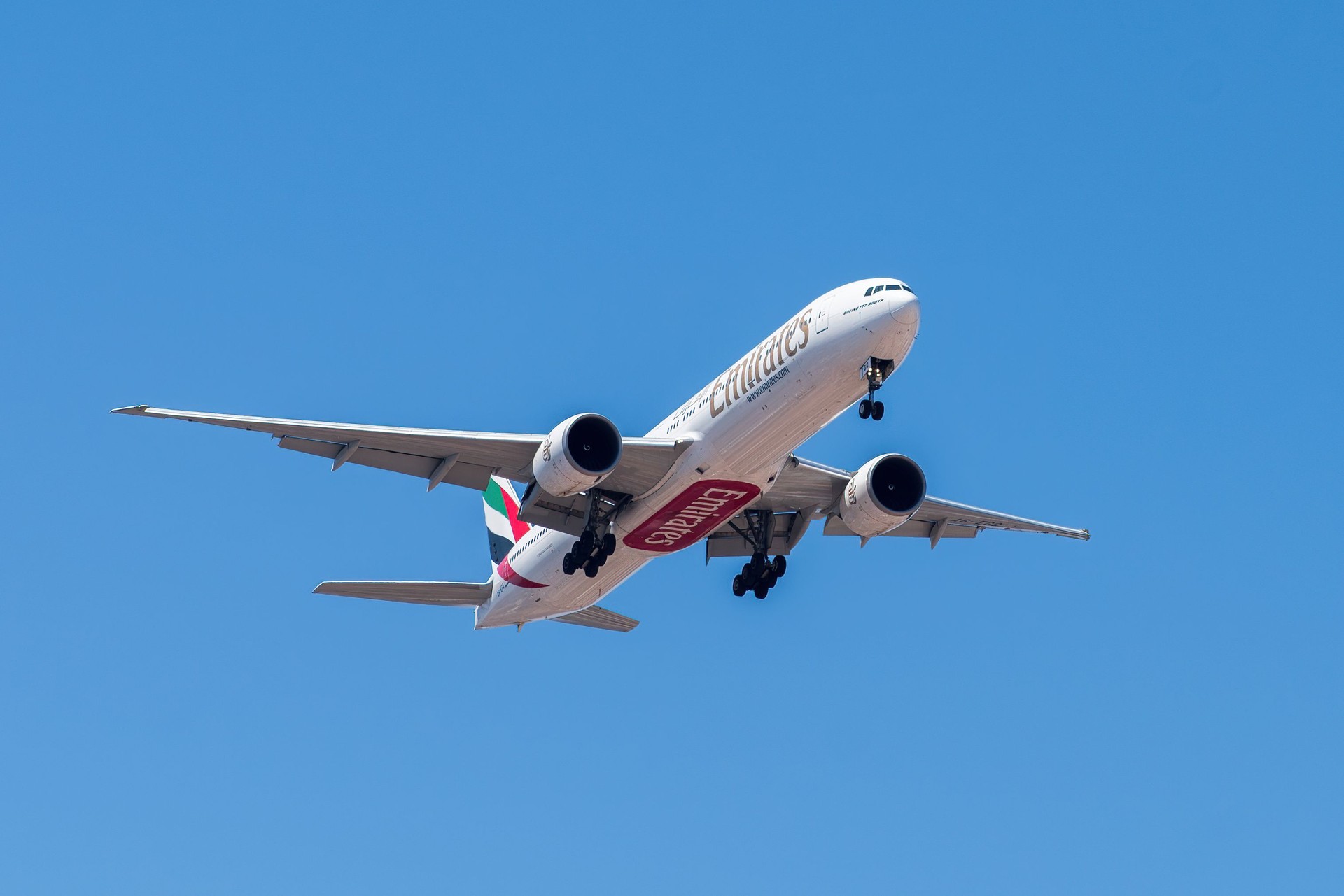 UAE based air company Emirates with aircraft Boeing 777-300ER approaching to land at Lisbon International Airport against blue sky